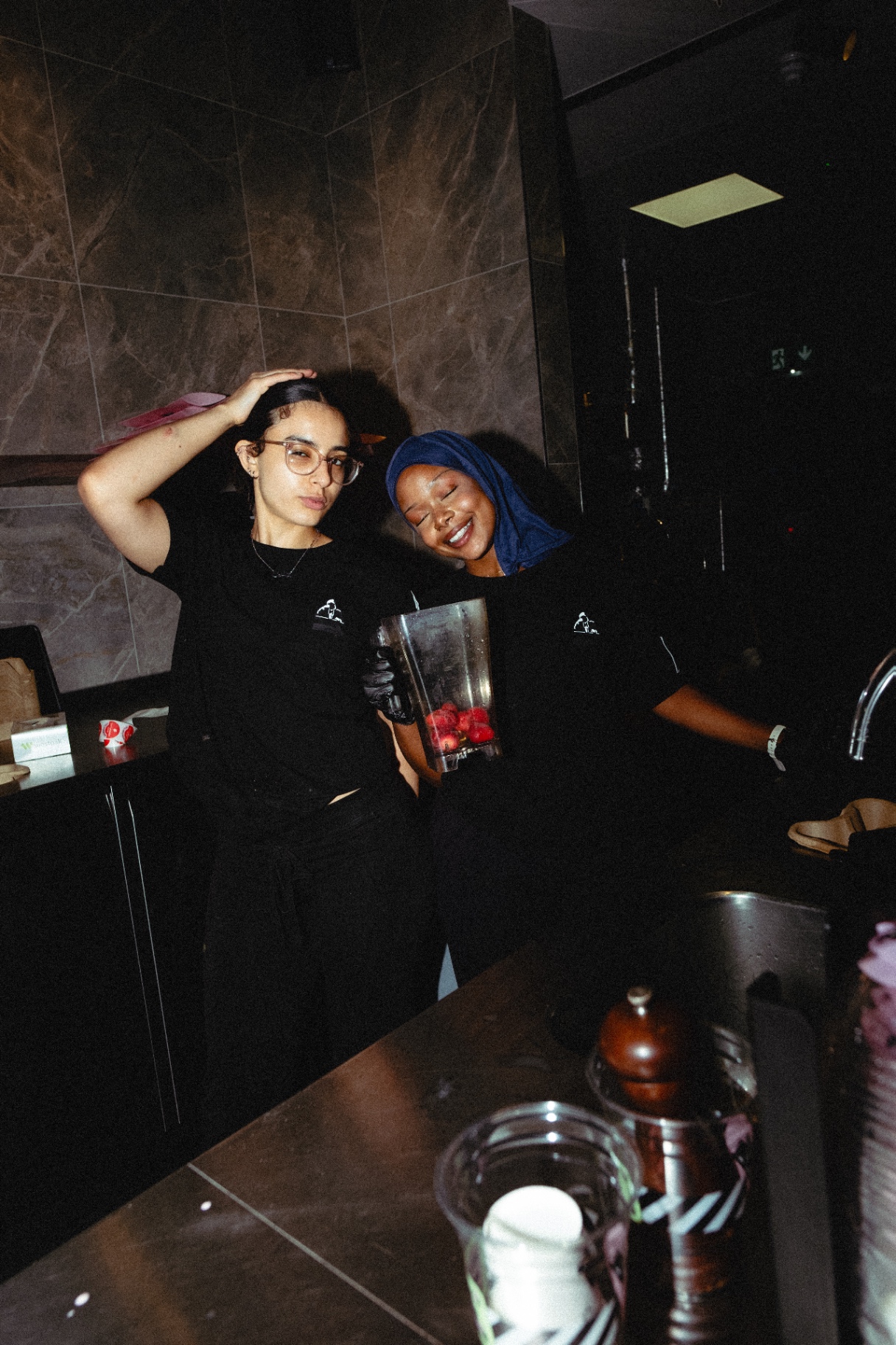 Two people indoors holding a blender with fruit